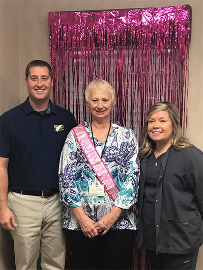 Two dental team members smiling with patient wearing a pink sash