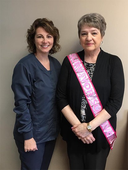 Dental team member smiling with a patient who is wearing a pink sash