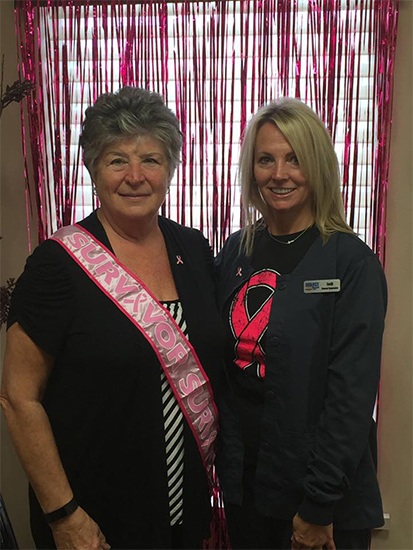 Smiling patient wearing a pink sash posing with dental team member