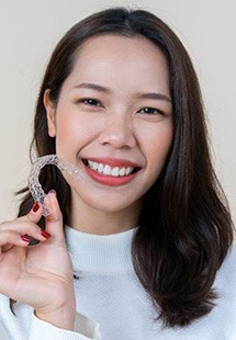 young woman smiling while holding Invisalign aligner