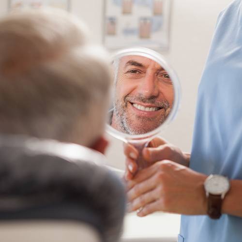 Man looking at his smile in mirror after dental care