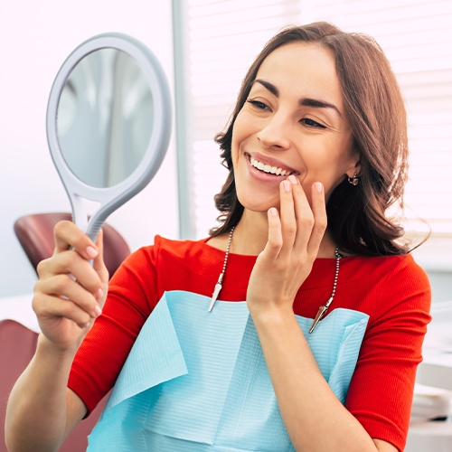 Woman looking at smile after metal free dental restoration treatment