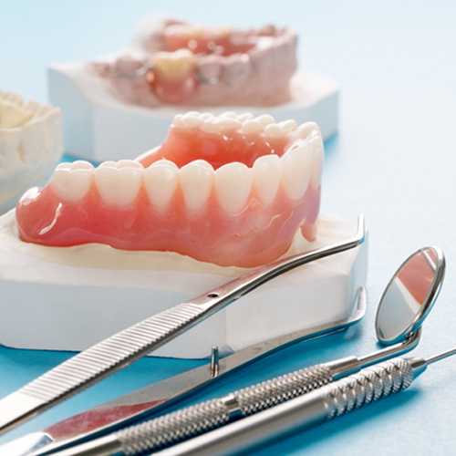 a plaster model of a mouth with a full denture over it and dental instruments sitting besides it