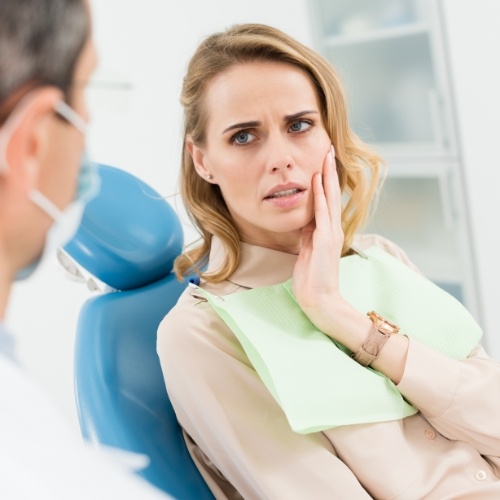 Woman holding cheek while talking to emergency dentist