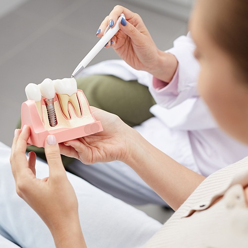 Dentist showing patient a dental implant and tooth model