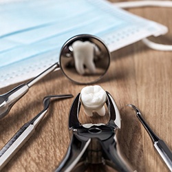 Dental forceps holding tooth on table next to face mask and dental mirror