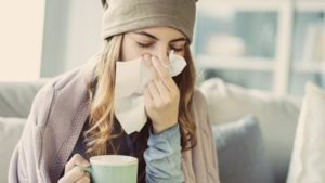 Woman holding a mug in one hand and holding a tissue to her nose with the other