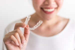 person smiling while holding Invisalign aligner 